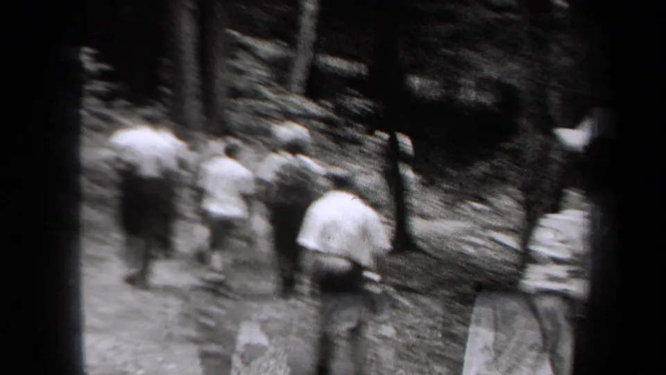 A softly focused rear view shows people walking through trees on a dirt path in 1938 New York footage.