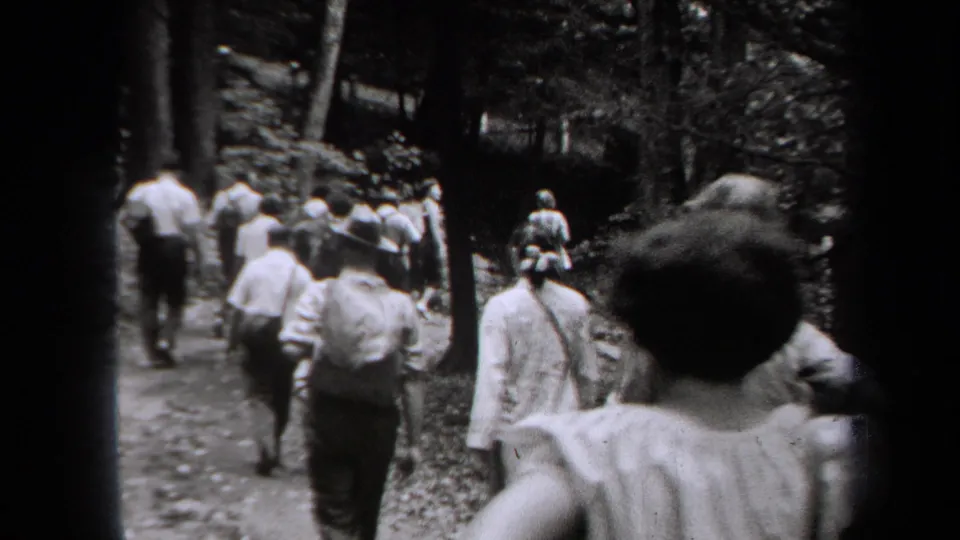 Men and women, including figures in hats and dresses, move away along a wooded trail in a 1938 New York home movie.