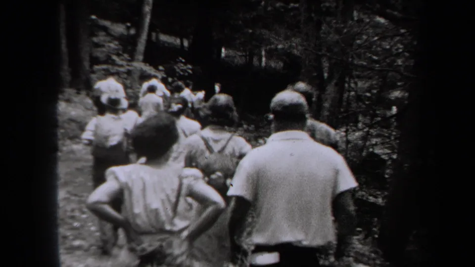 1938 New York home-movie frame showing a small group walking away on a wooded trail in black and white.
