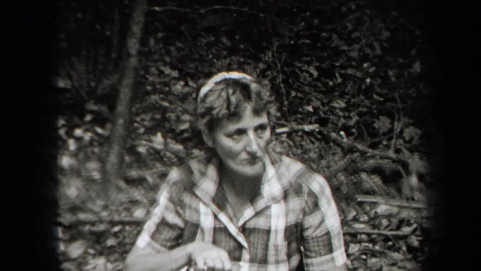 Black-and-white 1938 New York frame of a woman in a plaid dress looking off camera during a trail break.