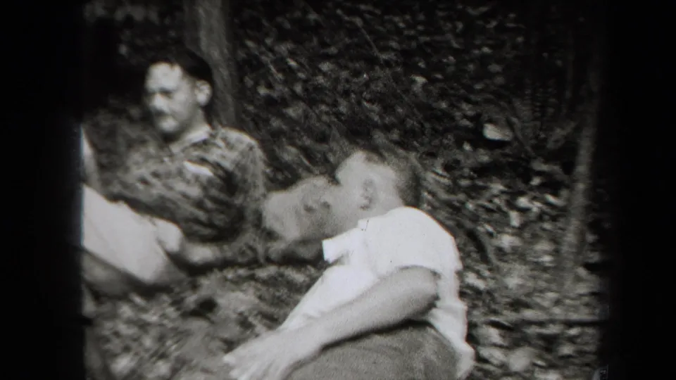 1938 New York home-movie frame showing adult friends seated informally in a wooded area, partly soft and grainy.