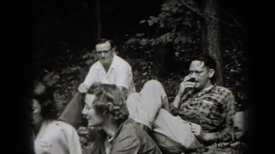 1938 New York home-movie frame of adult friends seated on leaves, including a man smoking and a woman in profile.
