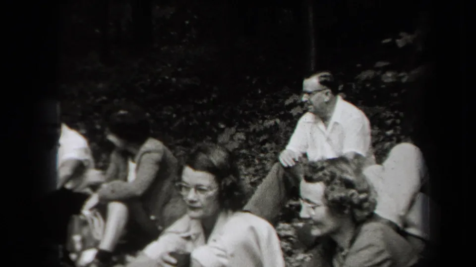 1938 New York home-movie frame of adults seated in a wooded area during a picnic, some facing the camera.
