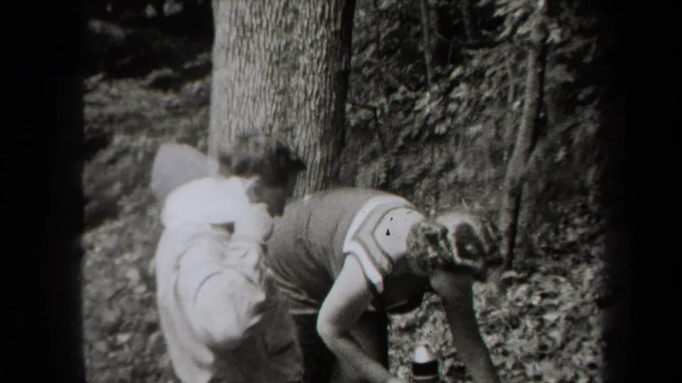 Two young men in a wooded New York setting appear to bend toward the ground during a 1938 outdoor home-movie moment.