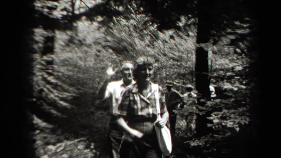 Adults in period clothing walk toward the handheld camera on a wooded path in black-and-white 1938 New York home-movie footage.