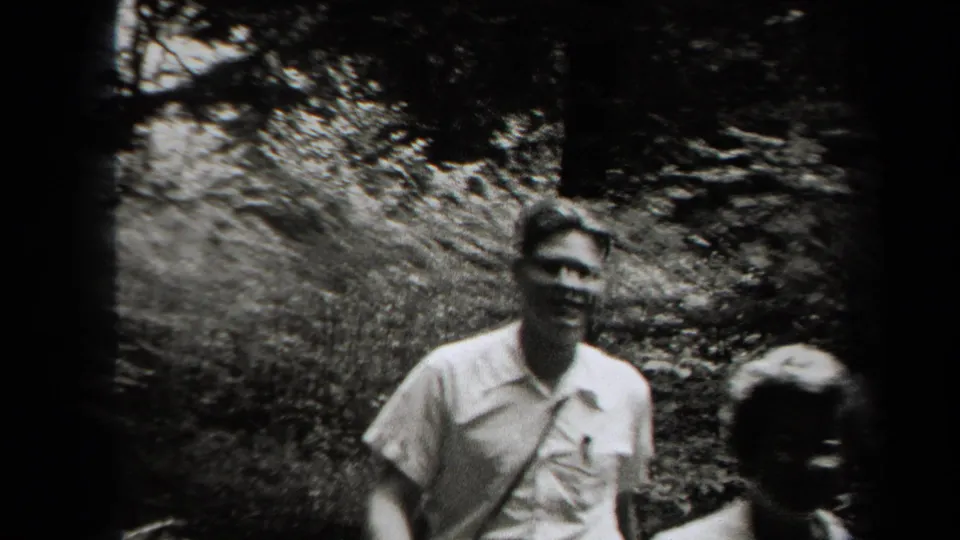 A young man in a light short-sleeve shirt passes close to the handheld camera during the New York woodland outing.