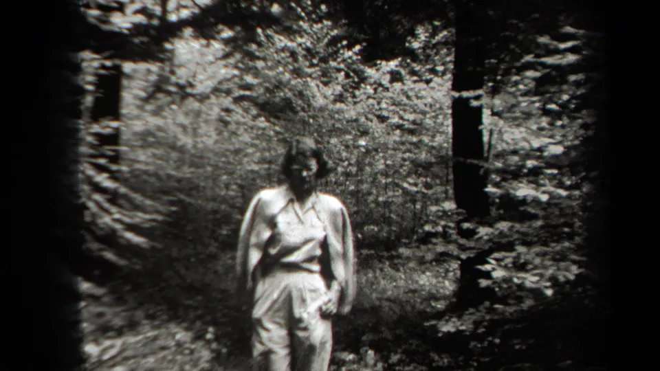 A woman in light sleeveless clothing walks along the wooded path in the 1938 New York home-movie scene.