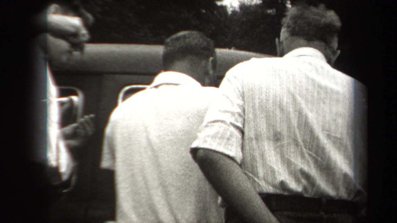 In 1938 New York home-movie footage, men gather beside a dark automobile, seen from behind in a tight black-and-white frame.