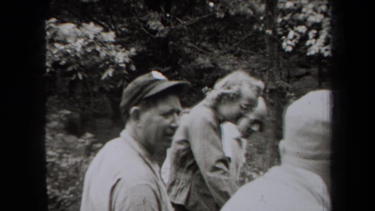 Adult men stand together outdoors near trees and rocks.