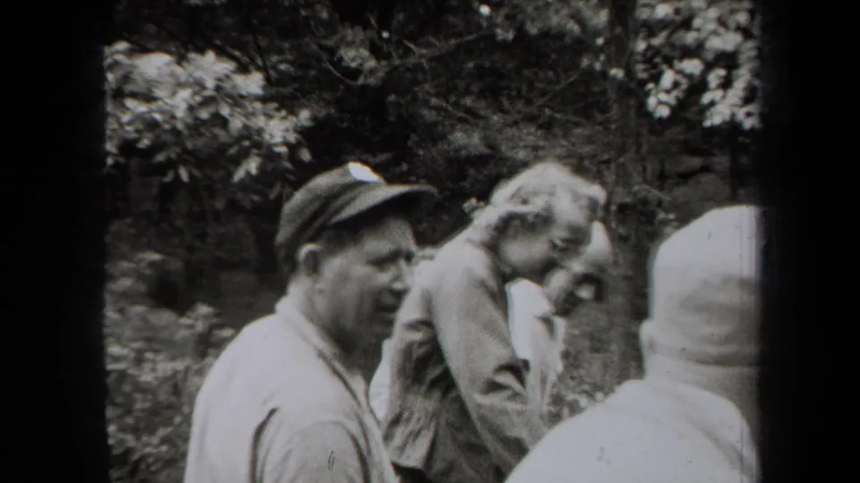 Black-and-white 1938 New York home-movie frame with adult men in caps and collared shirts gathered in woods.