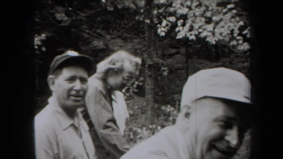 1938 New York 8mm frame showing adult men in casual clothing near a wooded bank, with one face close to camera.