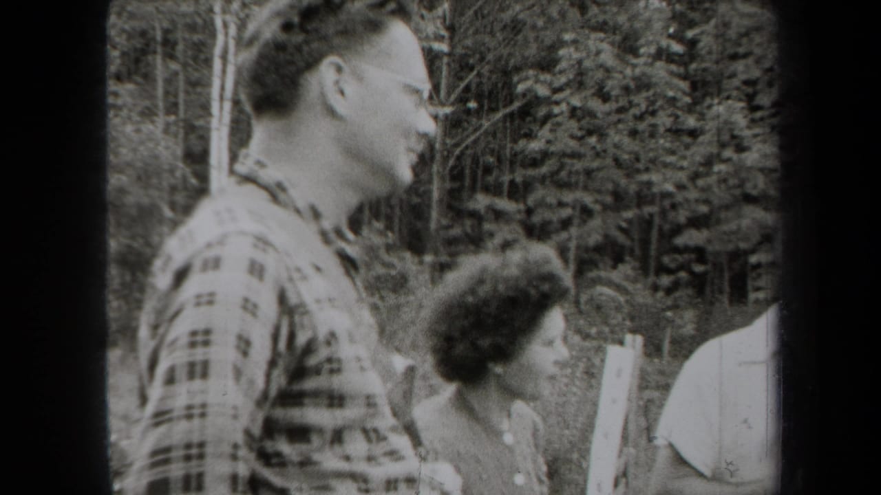 1938 New York home-movie frame showing adults talking outdoors near trees, led by a man in a plaid shirt and glasses.