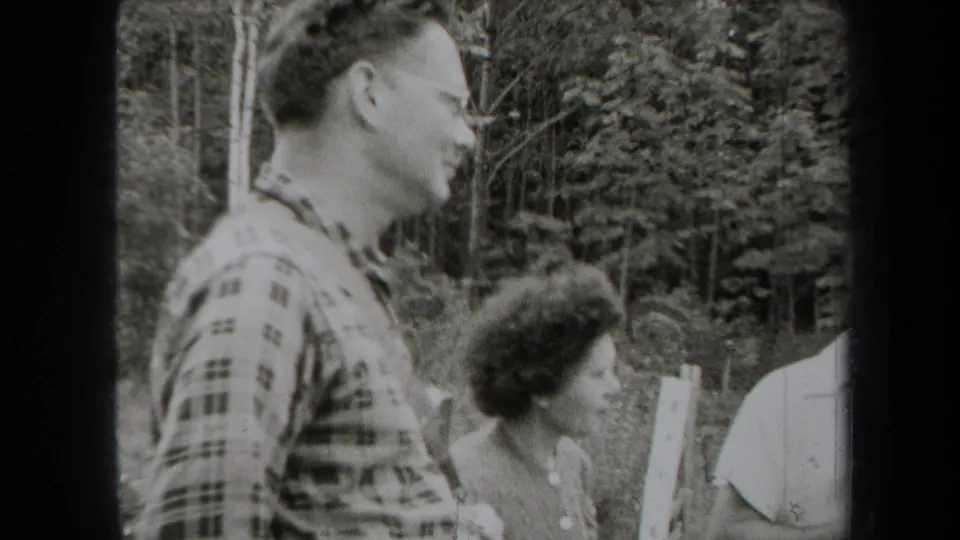 1938 New York home-movie frame showing adults talking outdoors near trees, led by a man in a plaid shirt and glasses.