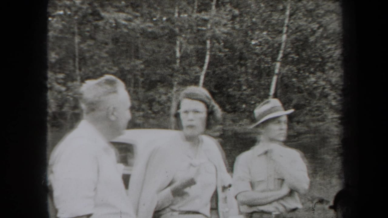 1938 New York home-movie frame showing adults in period clothing talking beside a car at the edge of woods.