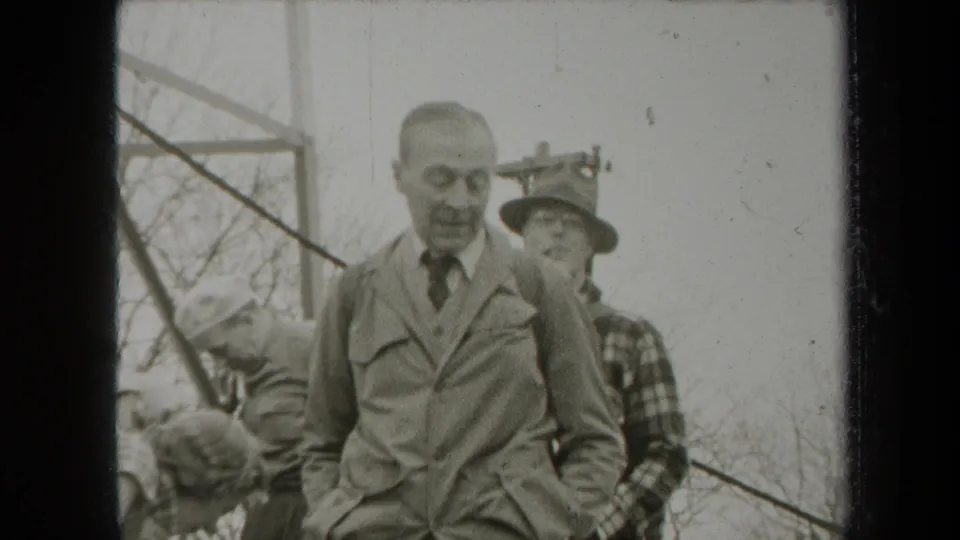 1938 New York home-movie frame showing two adult men in a wooded setting, with one man in a suit and tie near the camera.