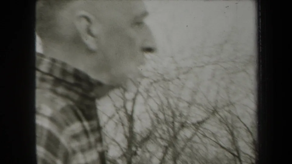 Soft 1938 New York home-movie frame showing a close side profile of an adult man in plaid with wooded background.