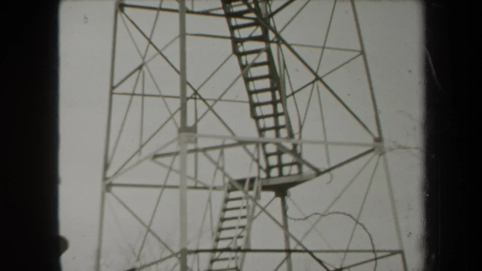 1938 New York home-movie frame of the tower's lower stairway and platform, with a faint visitor figure near the base.