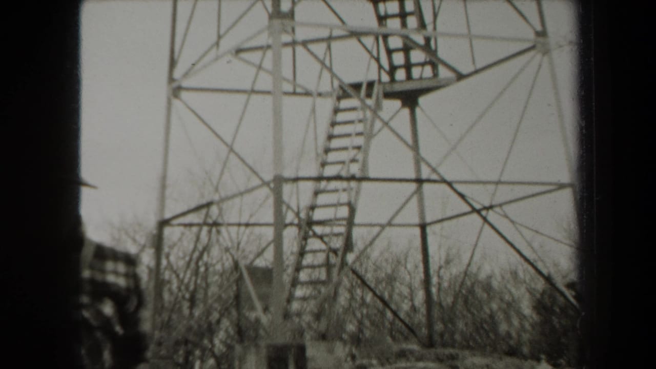 1938 New York 8mm frame showing a tall metal observation tower above leafless woods, with a partially visible person at the left edge.