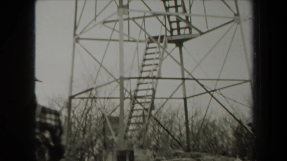 1938 New York 8mm frame showing a tall metal observation tower above leafless woods, with a partially visible person at the left edge.