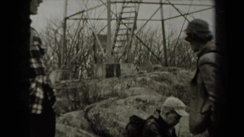 People in period coats and hats move through rocky New York woodland beneath a metal observation tower in this 1938 home-movie frame.