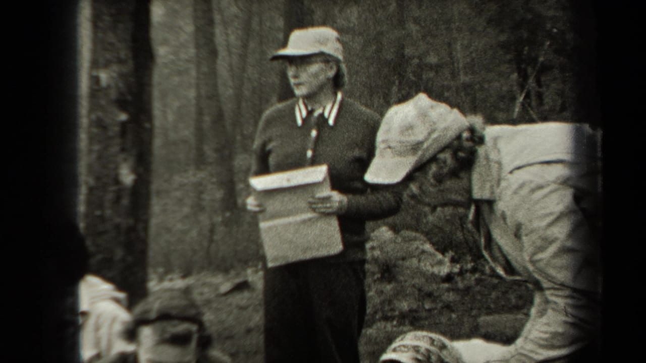Woman in cap holds a clipboard while others work near chickens outdoors.