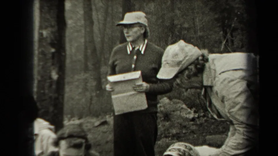 1938 New York home-movie frame showing a woman with a clipboard as people handle chickens on the ground nearby.