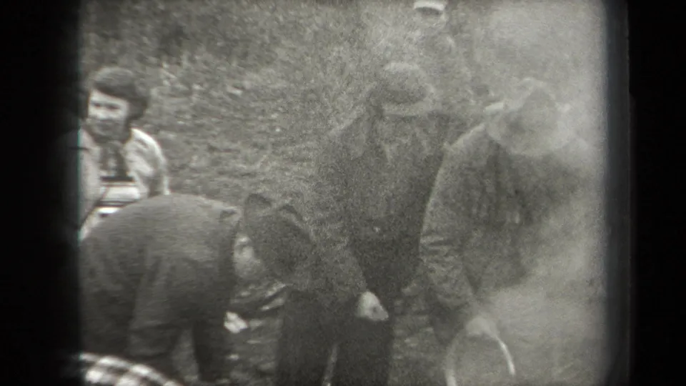 Grainy 1938 New York home-movie frame of men clustered around smoke or haze near a possible fire pit in the woods.