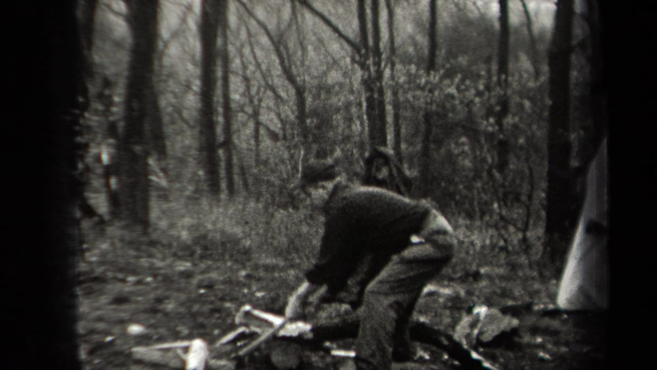 In 1938 New York home-movie footage, a man bends over kindling and logs in a wooded area as other men stand nearby.