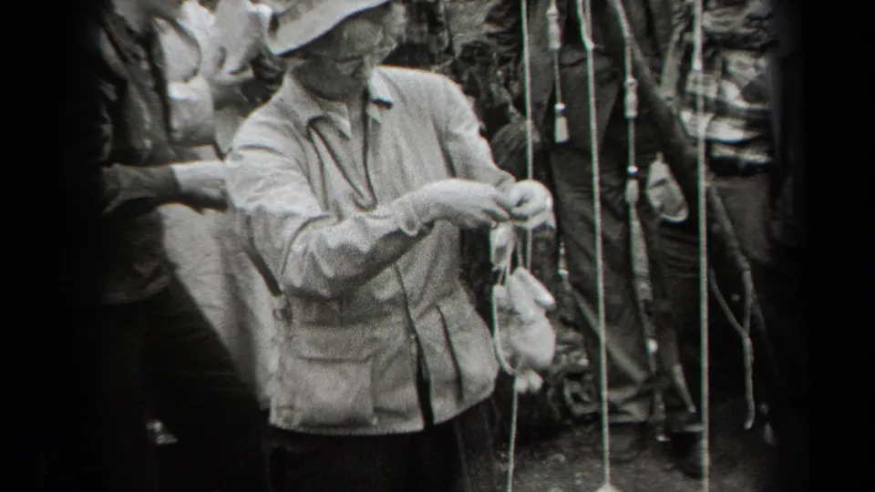A person in a light jacket and brimmed hat tends suspended chickens in 1938 New York outdoor home-movie footage.