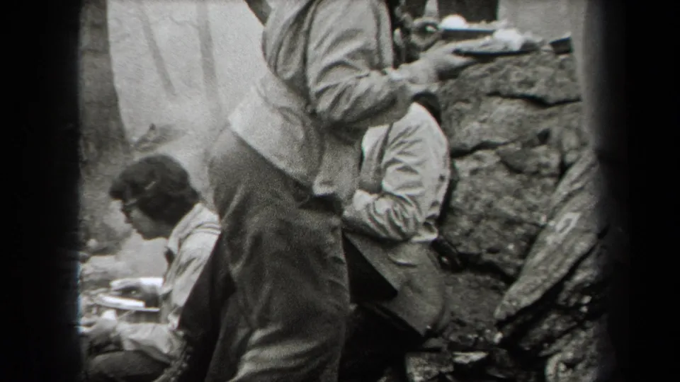 1938 New York home-movie frame showing people seated on rocks near outdoor food preparation, with faces partly visible.