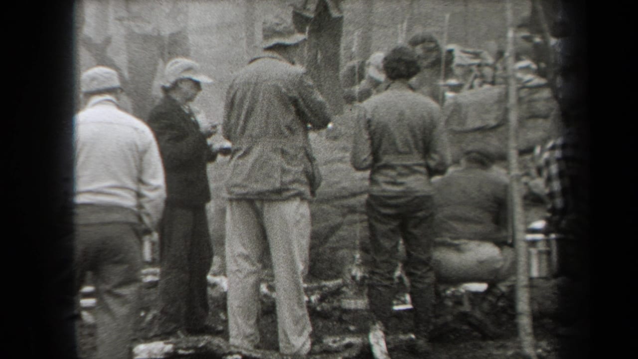 Adults in period hats and jackets gather around an outdoor cooking area in wooded New York home-movie footage from 1938.