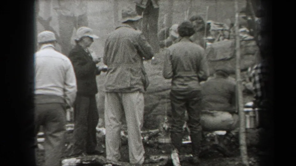 Adults in period hats and jackets gather around an outdoor cooking area in wooded New York home-movie footage from 1938.