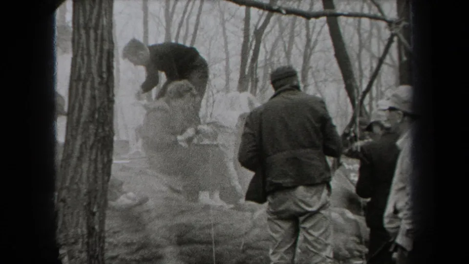 Adults in hats and jackets move around a smoky wooded cooking area in 1938 New York home-movie footage.