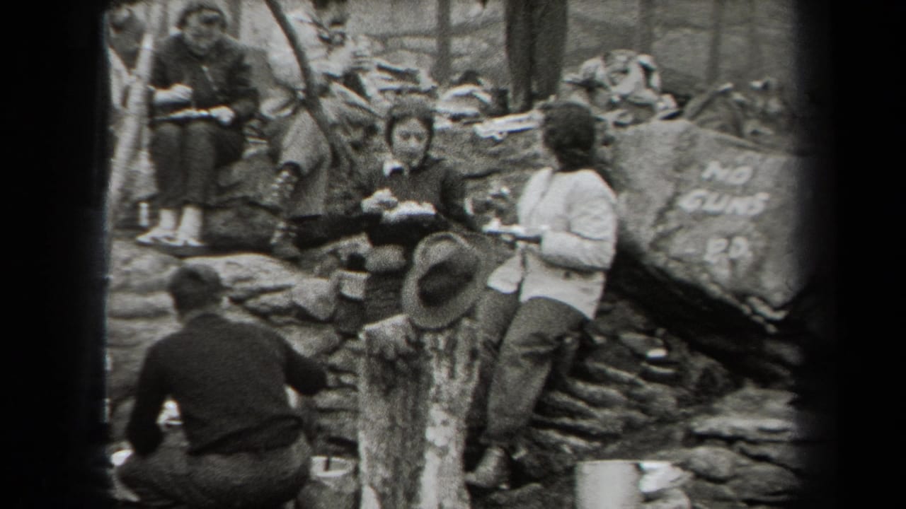 1938 New York home-movie frame showing campers eating near rocks, trees, smoke, and a large stone marked NO GUNS.