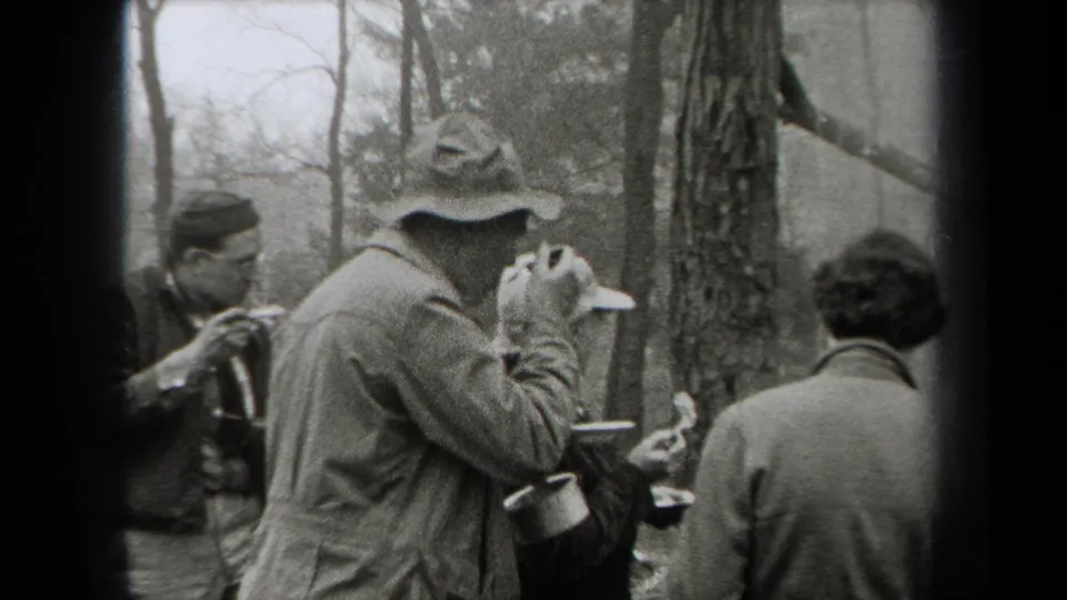 A small group of hikers in 1938 New York stands among trees, with one person drinking from a cup and others holding outdoor gear.