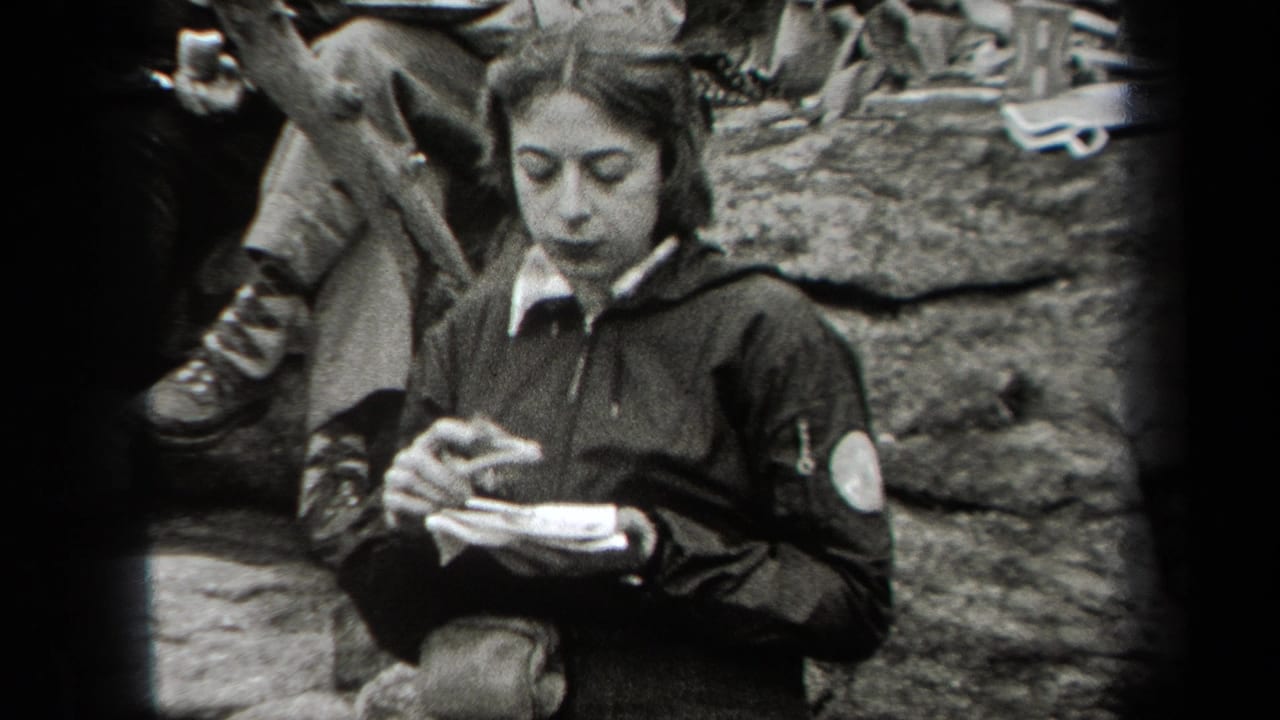 Young woman seated outdoors eating from a small plate beside rocks and other seated people.