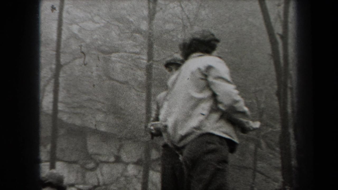 Black-and-white 1938 New York home-movie frame showing men in jackets among bare trees and rocks outdoors.