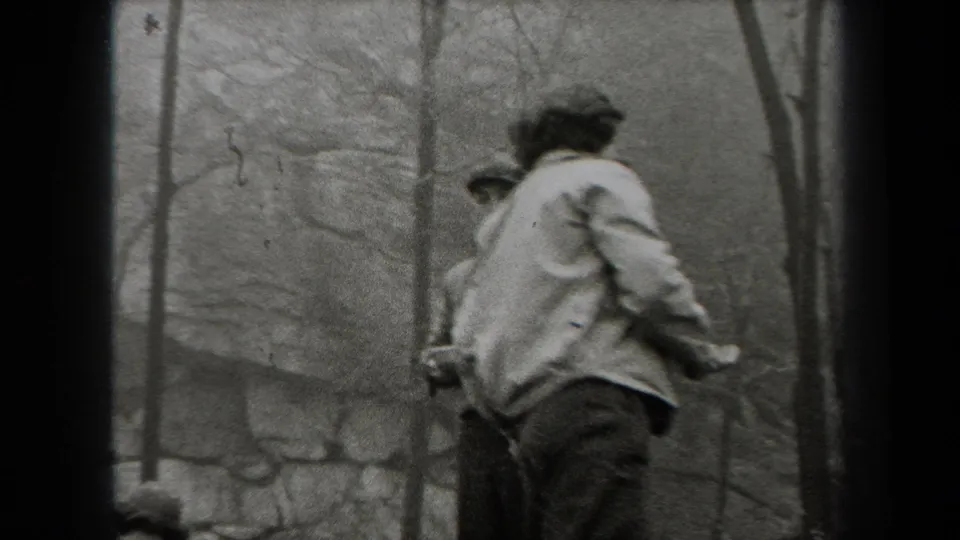 Black-and-white 1938 New York home-movie frame showing men in jackets among bare trees and rocks outdoors.