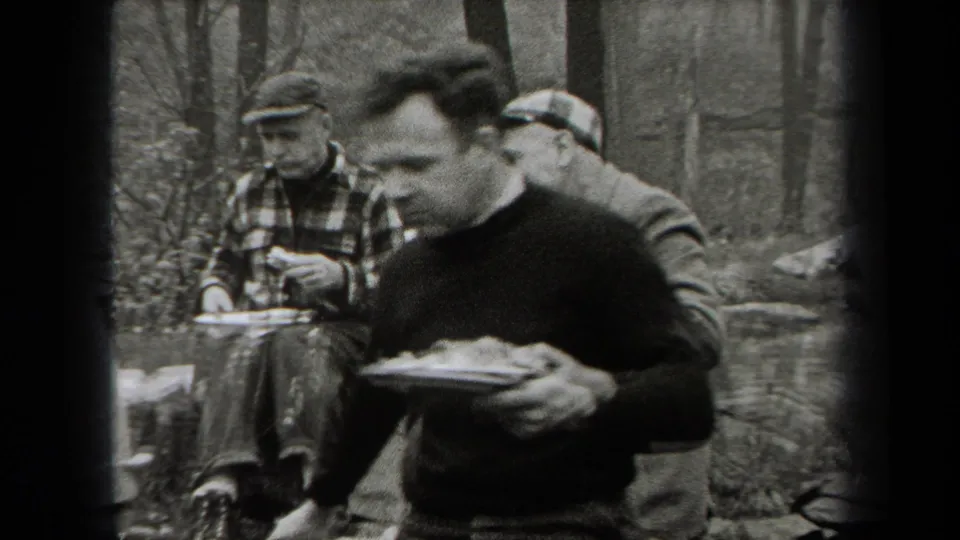 Black-and-white 1938 New York frame showing men eating from plates, including one man close to the camera.