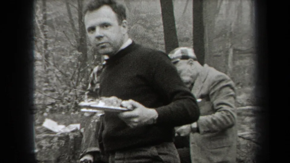 1938 New York home-movie frame showing men eating outdoors in a forested mountain setting.