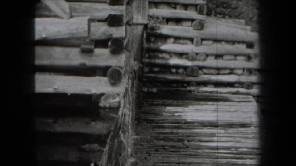 Black-and-white 1938 home-movie frame showing log construction details and a weathered wooden walkway.