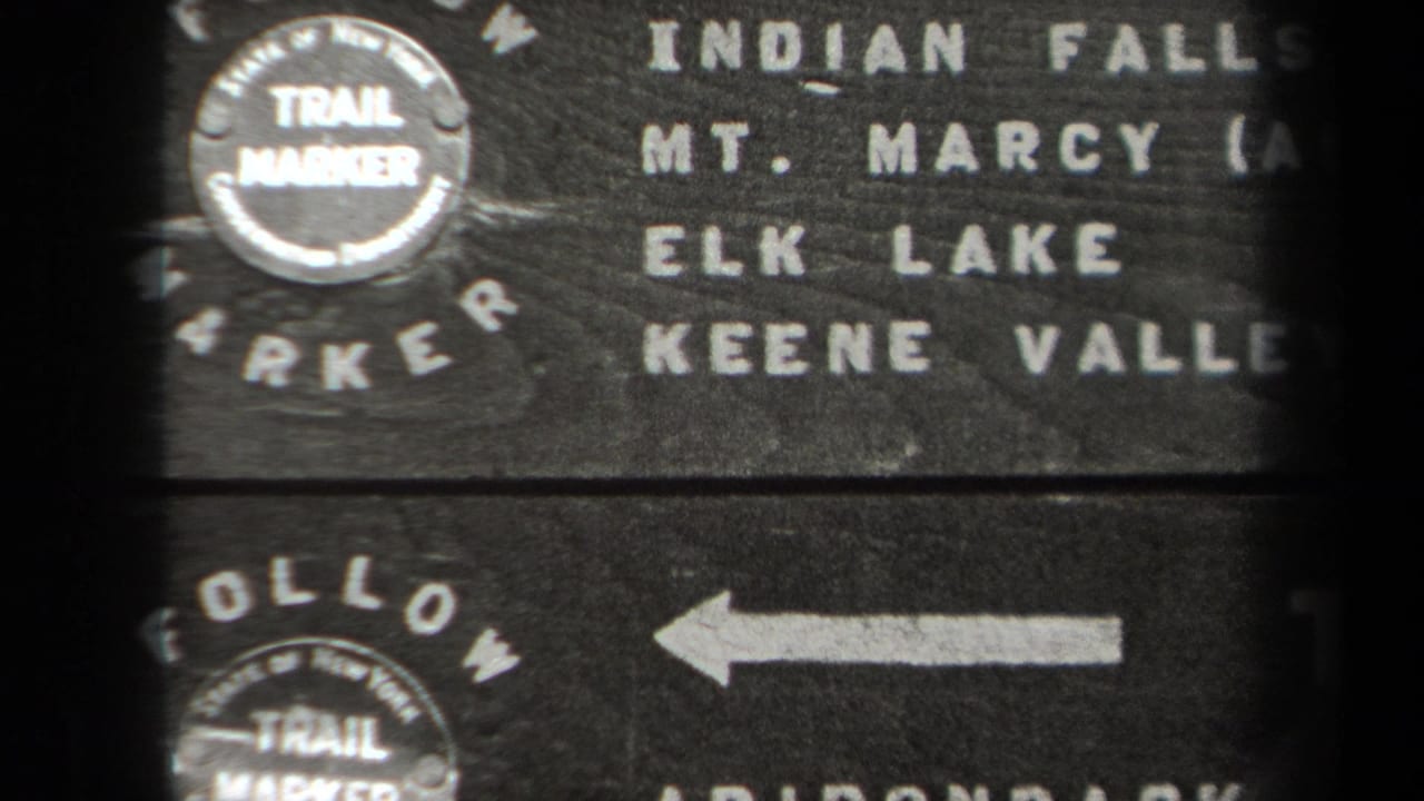 1938 New York 8mm frame showing a weathered wooden trail marker with Indian Falls, Mt. Marcy, Elk Lake, and Keene Valley text.