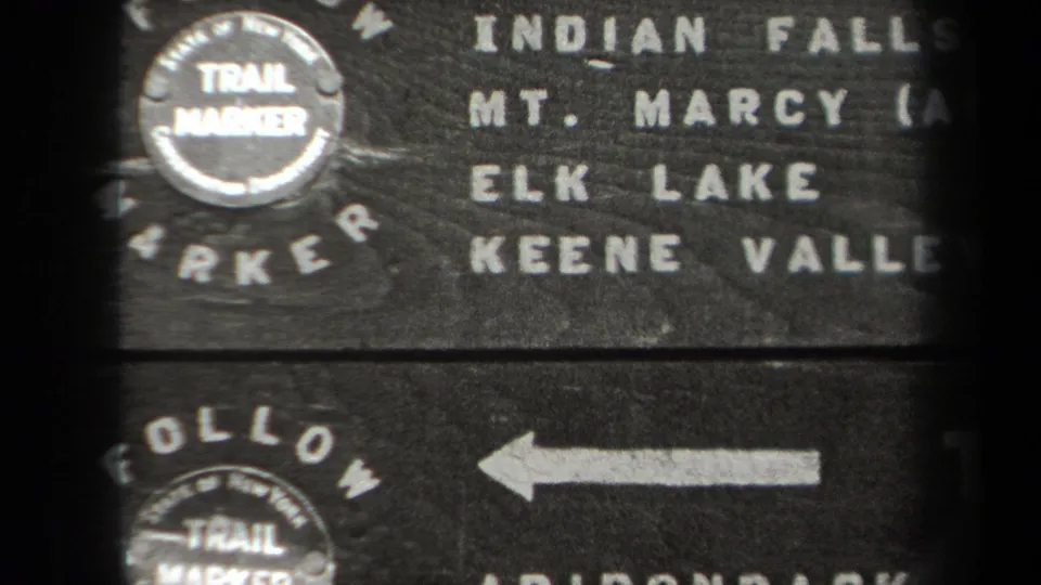 1938 New York 8mm frame showing a weathered wooden trail marker with Indian Falls, Mt. Marcy, Elk Lake, and Keene Valley text.