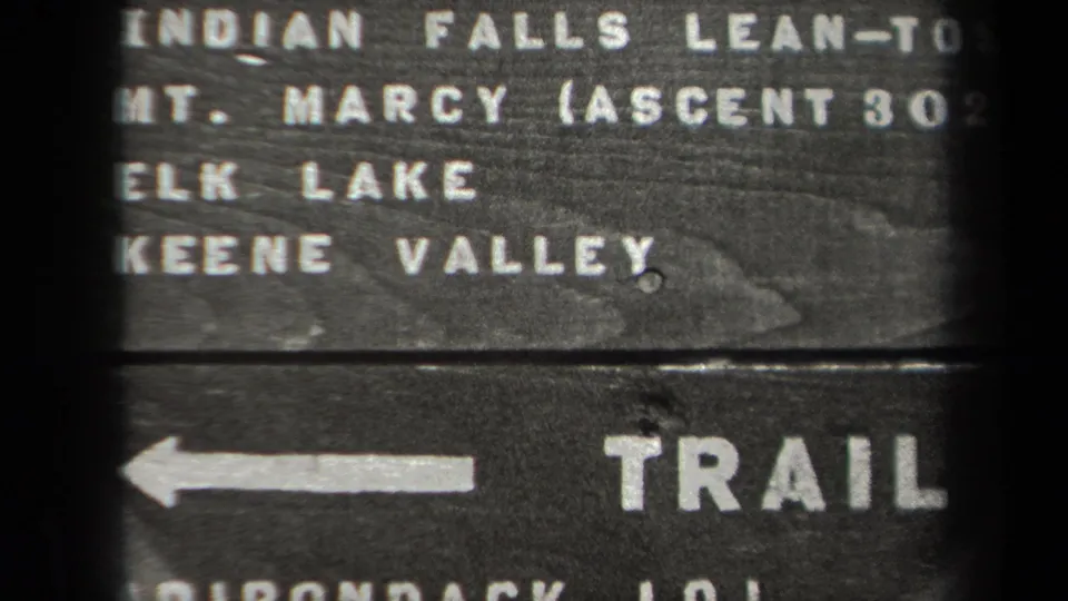 1938 New York frame showing a close-up of a wooden trail marker with a left arrow, destination lettering, and mile distances.