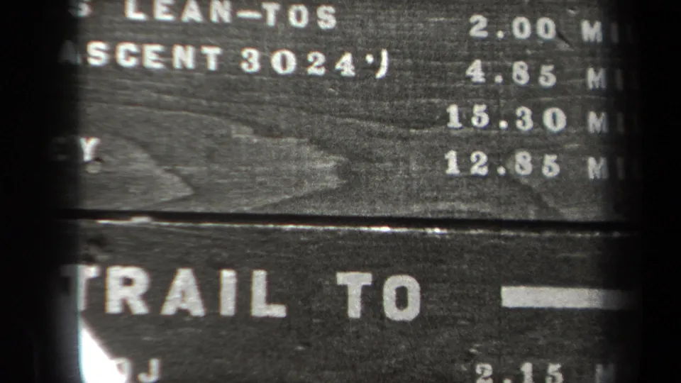 1938 New York 8mm frame showing a tight, soft-focus view of the trail marker with arrows, mileages, and Trail To lettering.