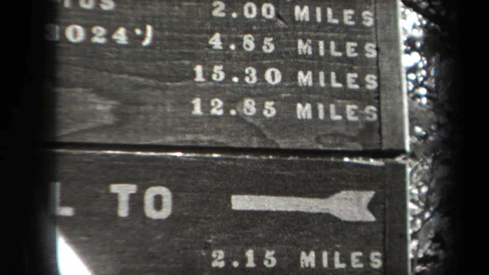1938 New York 8mm frame showing a weathered wooden trail marker with white mileage figures and directional arrows in a wooded setting.