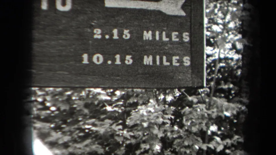Close 1938 Adirondack trail-sign view with bold mileage lettering and foliage below the sign board.