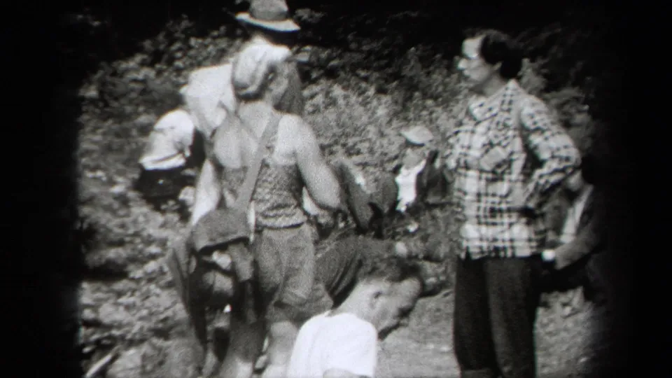 1938 New York home-movie frame showing a family hiking group on a wooded Adirondack path, with hats, suspenders and a plaid shirt visible.