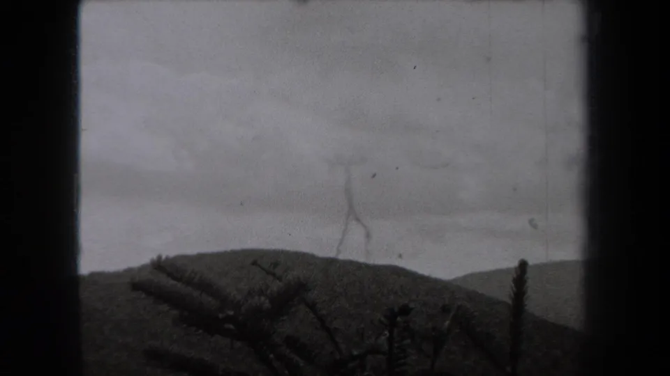 1938 New York home-movie frame showing a soft mountain ridge, overcast sky, and silhouetted evergreen branches within 8mm borders.