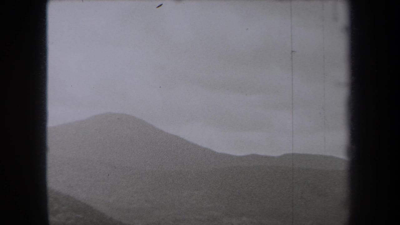 1938 New York home-movie frame showing layered hills under a heavy gray sky, bordered by dark film edges.